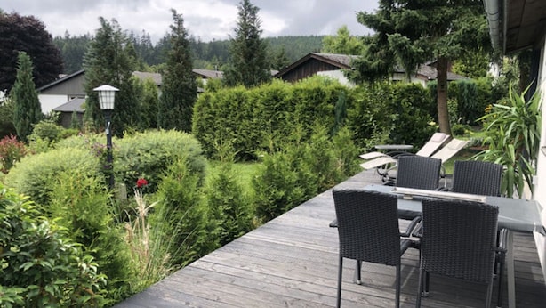 A wooden deck with outdoor furniture, surrounded by lush greenery and residential buildings in the background. - Holiday Home Kent Comfortable Vacation Home (Willingen)
