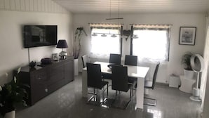 A modern dining area with a white table and black chairs, a flat-screen TV mounted on the wall, and a ceiling fan. - Holiday Home Kent Comfortable Vacation Home (Willingen)