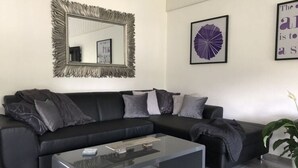 A modern living room with a black sectional sofa, a glass coffee table, and a decorative mirror. - Holiday Home Kent Comfortable Vacation Home (Willingen)