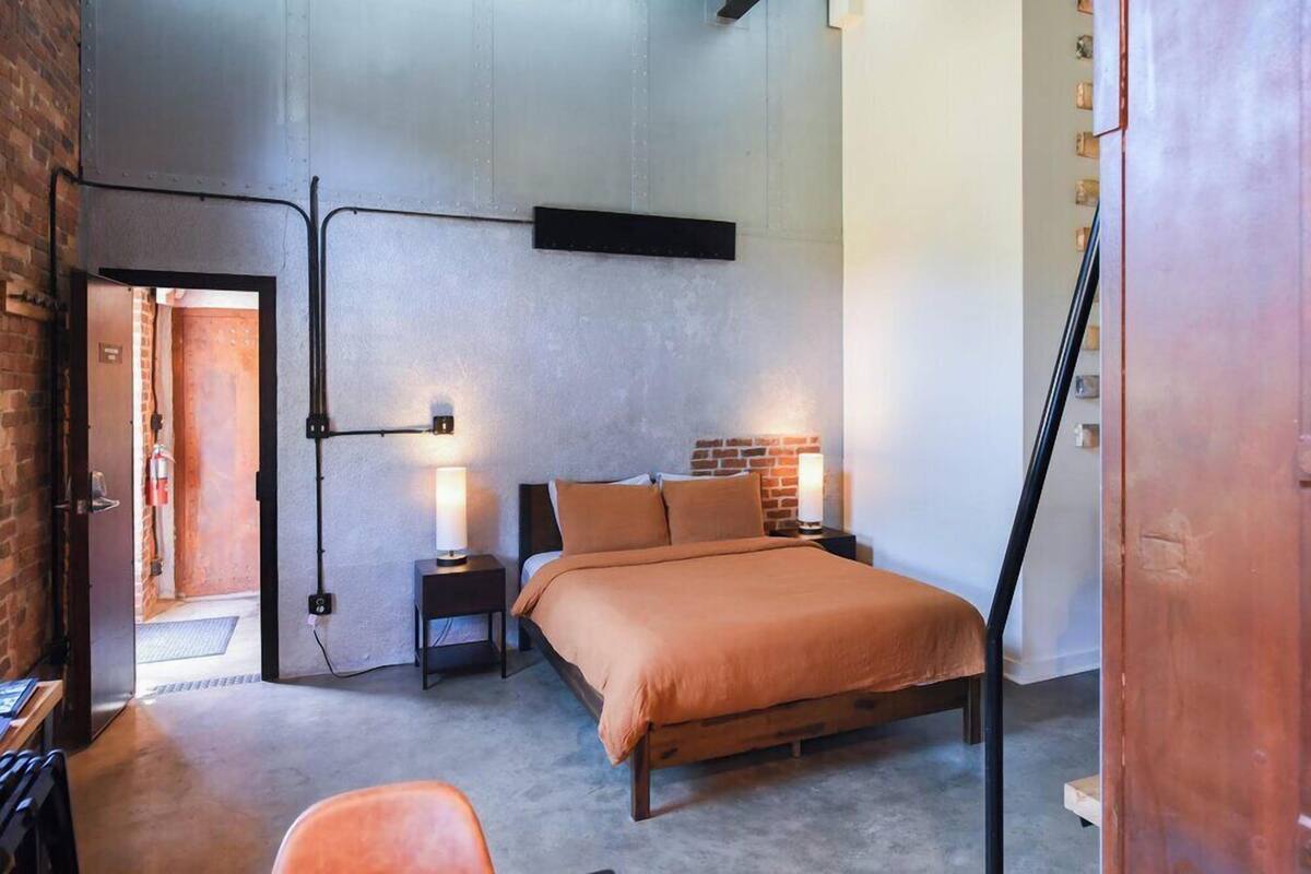 A bedroom with a bed, nightstands, a brick accent wall, and a door leading to another room.