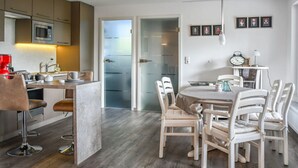 Una cocina moderna con una isla central, un comedor con sillas blancas y un refrigerador al fondo.