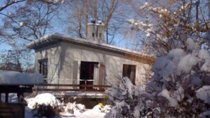Uma cabana de madeira com varanda, rodeada por neve na terra e nas árvores.