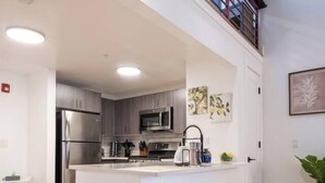 A modern kitchen with a central island, stainless steel appliances, and white bar stools. - Classic Loft King Bed 30 min NYC (East Orange)