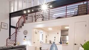 A modern living room with a dining area, a staircase, and a kitchen in the background. - Classic Loft King Bed 30 min NYC (East Orange)