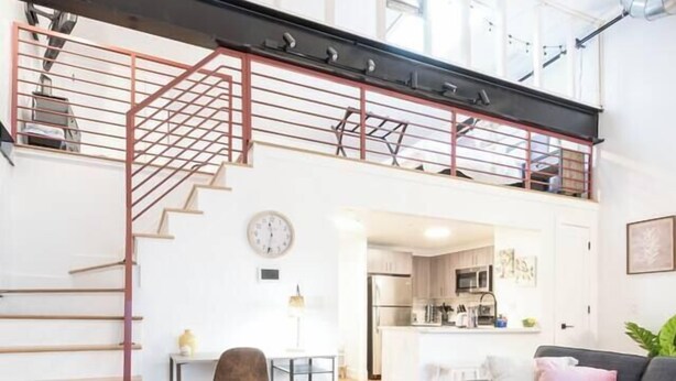 A spacious loft apartment with a high ceiling, exposed ductwork, a staircase, a kitchen, and a living area with a sofa and coffee table. - Classic Loft King Bed 30 min NYC (East Orange)