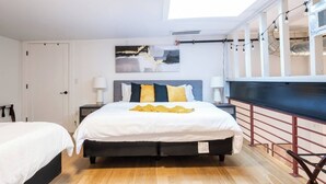 A bedroom with a bed, bedside tables, a skylight, and a view of the outside. - Classic Loft King Bed 30 min NYC (East Orange)