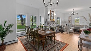 A spacious living room with a dining area, large windows, and a chandelier.