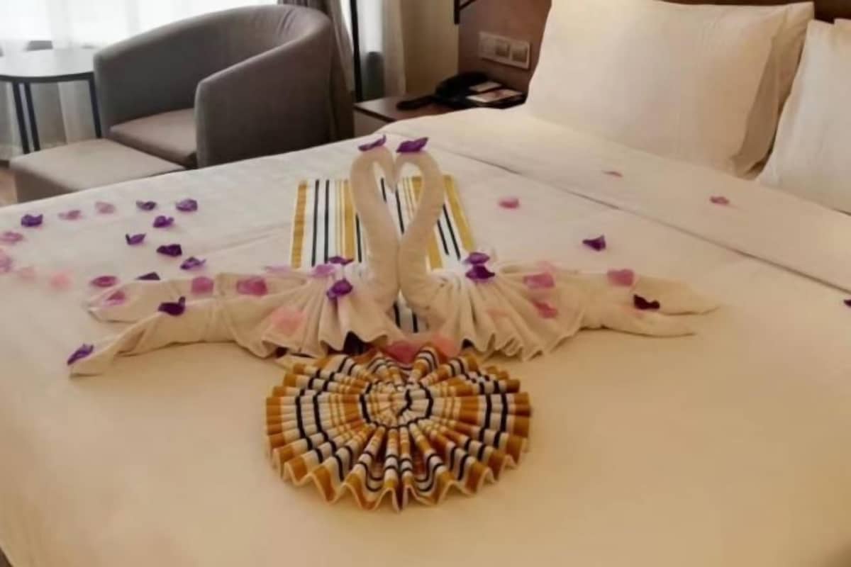 Ein Hotelzimmer mit einem ordentlich bezogenem Bett, einer herzförmigen Handtuchgestaltung und einem runden Handtuchmotiv auf dem Bett.