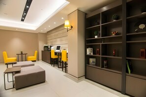 Ein moderner Lounge-Bereich mit gelben Sesseln, einer Couch, einem Schreibtisch mit Computer und einem Bücherregal mit verschiedenen Gegenständen.