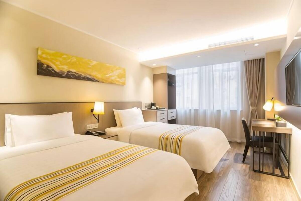 A hotel room with two beds, a desk, a chair, a TV, and a window with curtains.
