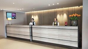 A reception desk with two staff members, a digital display, and a vase with flowers. - Homeinn Plus Hotel (Beijing Zhongguancun East Road) (Beijing)