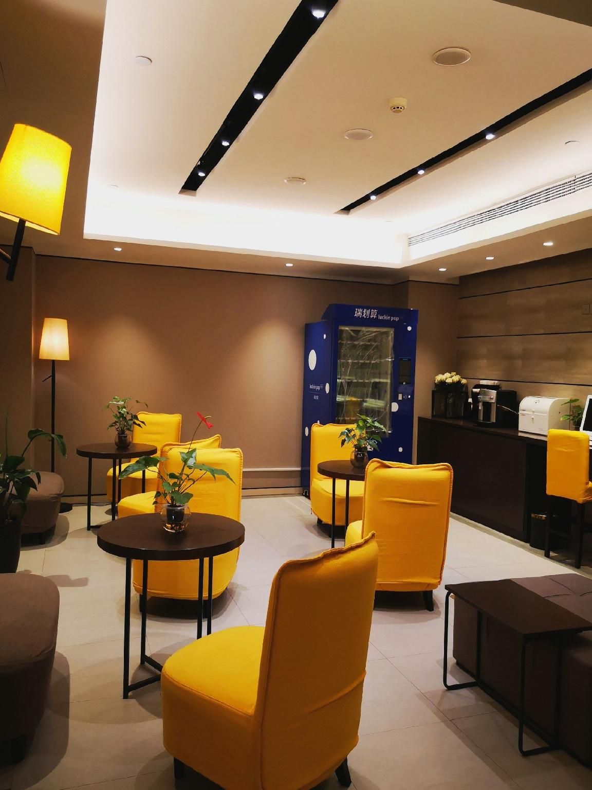 Un moderno vestíbulo de hotel con sillones amarillos, una recepción y una máquina expendedora azul.