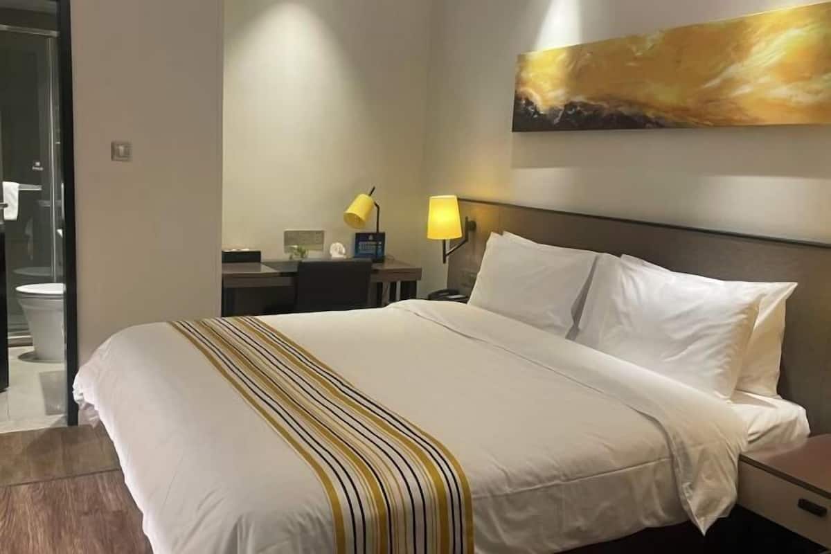 A hotel room with a large bed, a desk, a chair, a nightstand, a lamp, and a painting on the wall.