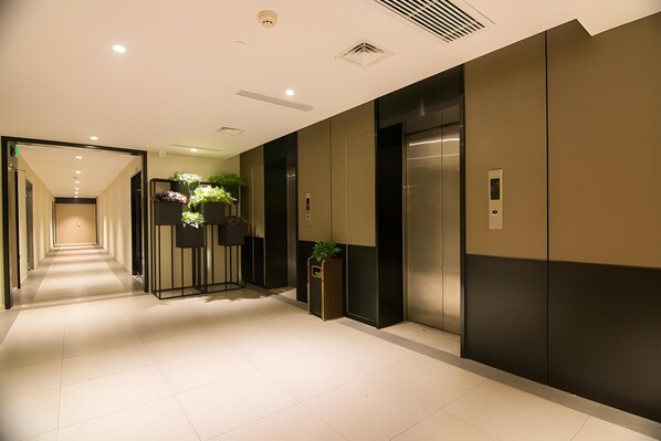 A hotel corridor with a modern design, featuring a long hallway, elevators, and a reception area with a plant. - Homeinn Plus Hotel (Beijing Zhongguancun East Road) (Beijing)