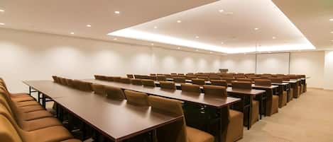 A conference room with multiple tables and chairs, recessed ceiling lighting, and a carpeted floor.