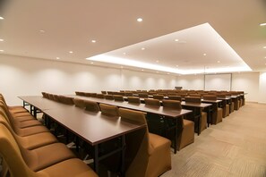 Ein Konferenzraum mit mehreren Tischen und Stühlen, deckenhohen Leuchten und einem Teppichboden.