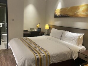 Ein Hotelzimmer mit Bett, Schreibtisch, Stuhl, Lampe und einem Bild an der Wand.