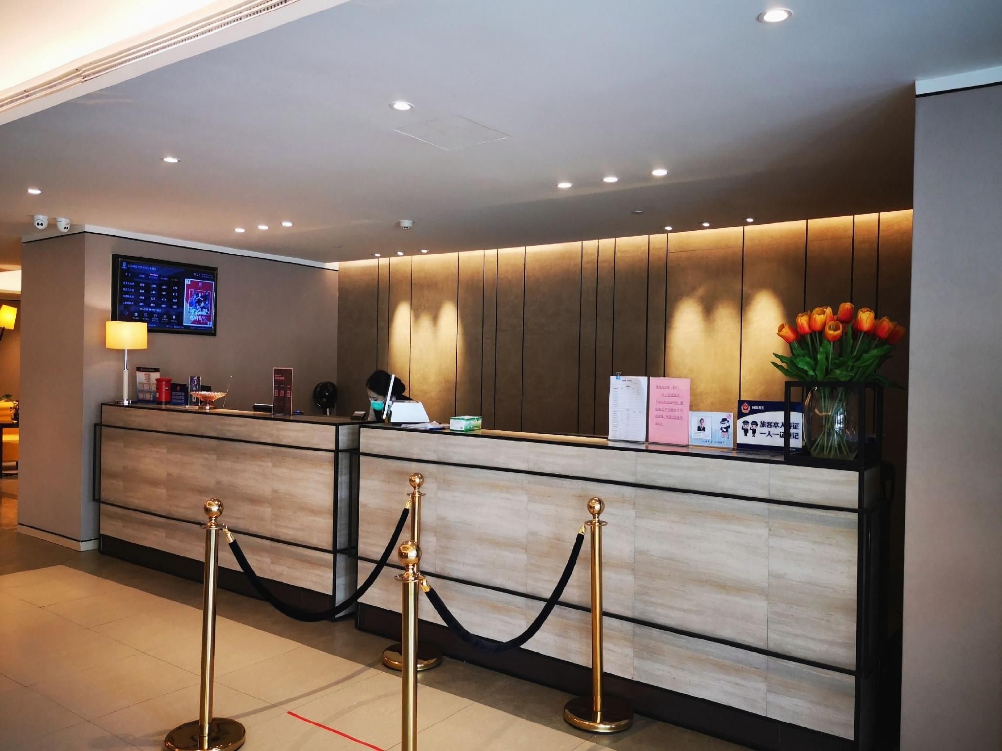 Un mostrador de recepción de hotel con una pantalla digital, una barra de recepción y un florero con flores.