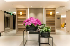Eine moderne Lobby mit zwei Zimmerpflanzen, einer Bank und einer Rezeption.