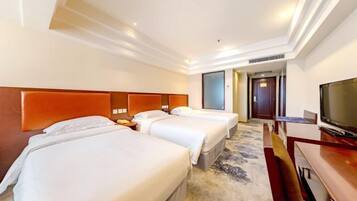 A hotel room with three beds, a television, and a carpeted floor.