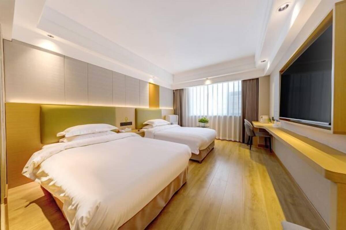 A hotel room with two beds, a desk, a chair, a large window with curtains, and a TV.