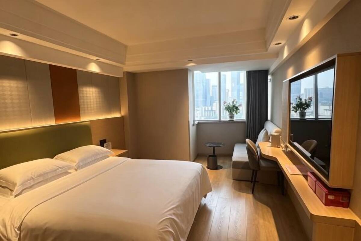 A hotel room with a bed, a desk, a chair, a TV, and a window with a city view.