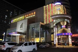 Un hotel con una entrada destacada, varios espacios de estacionamiento y un gran cartel iluminado.