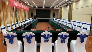 Une salle de conférence avec une longue table, des chaises blanches ornées de rubans bleus et une banderole rouge accrochée au mur.