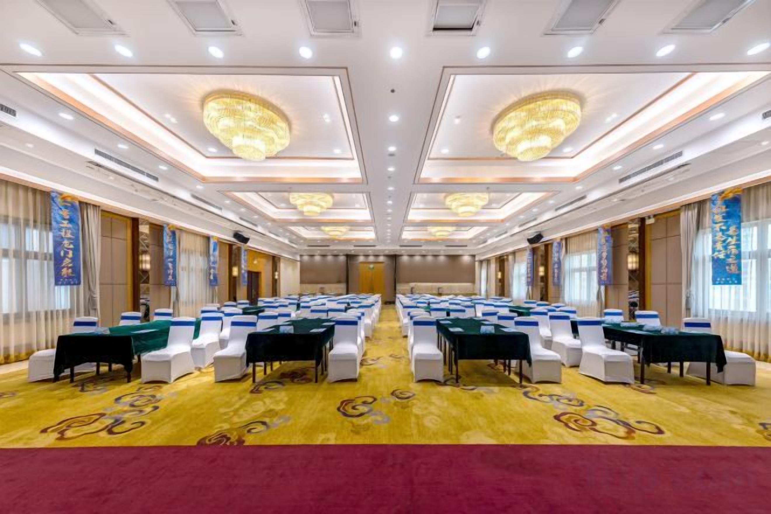 A conference room with rows of tables and chairs, a carpeted floor, and a chandelier.