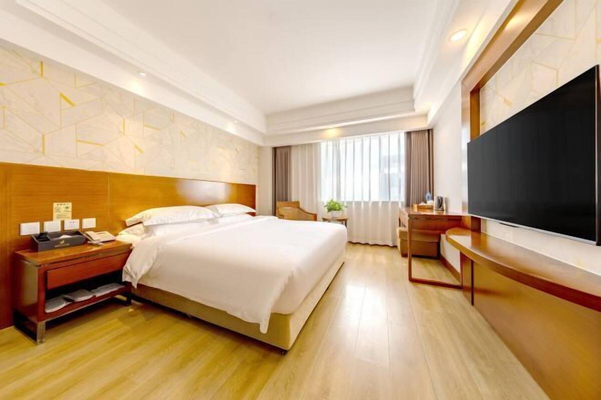 A hotel room with a bed, bedside table, TV, and a desk with a chair.