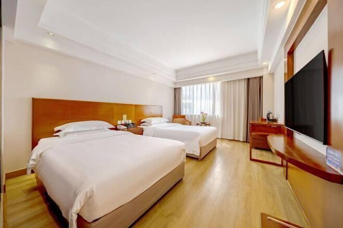A hotel room with two beds, a TV, and a wooden floor.