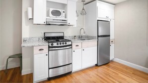 Une cuisine de taille réduite avec des meubles blancs, une cuisinière en acier inoxydable et un réfrigérateur.