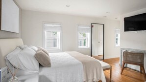 A bedroom with a bed, a chair, a television, and windows. - Jade Suite at The Hygge House (Newburyport)