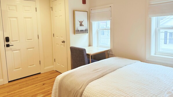 Un dormitorio con cama, escritorio y silla. Se observan dos puertas y una ventana.