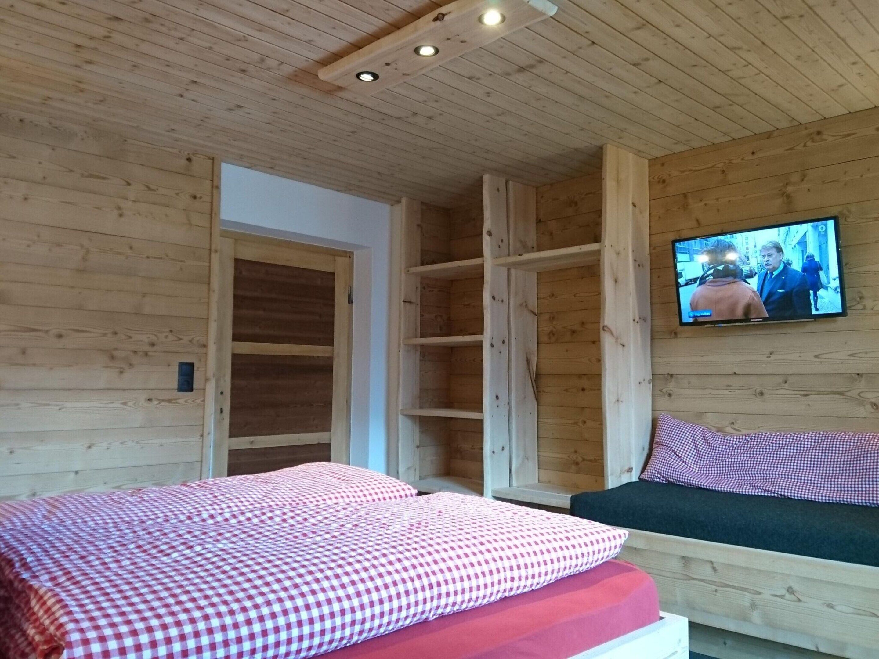 Habitación de cabaña de madera con dos camas, un televisor en la pared y un estante de madera.
