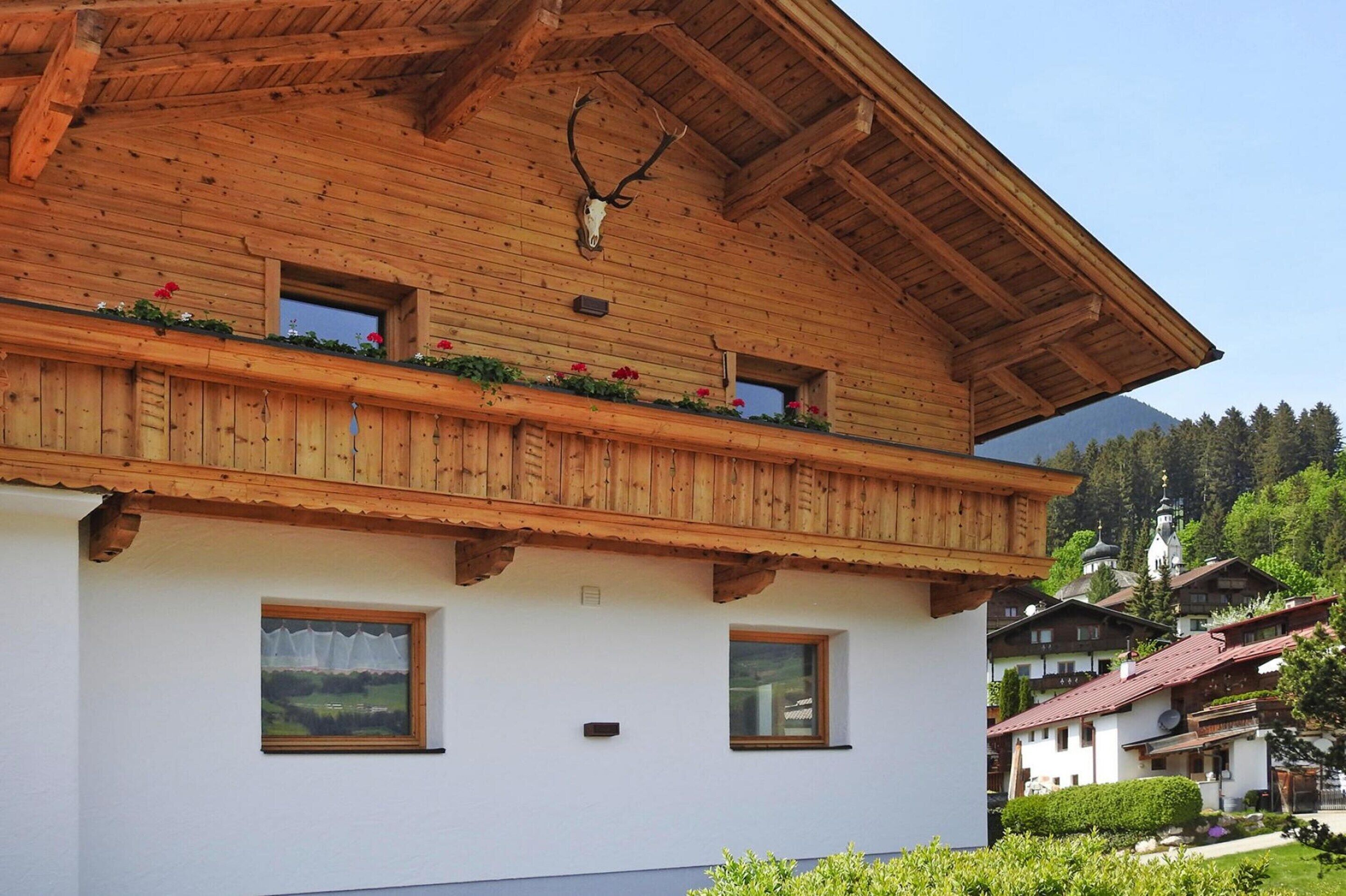 Een houten chalet met balkon, decoratie van een herten schedel en een berg op de achtergrond.