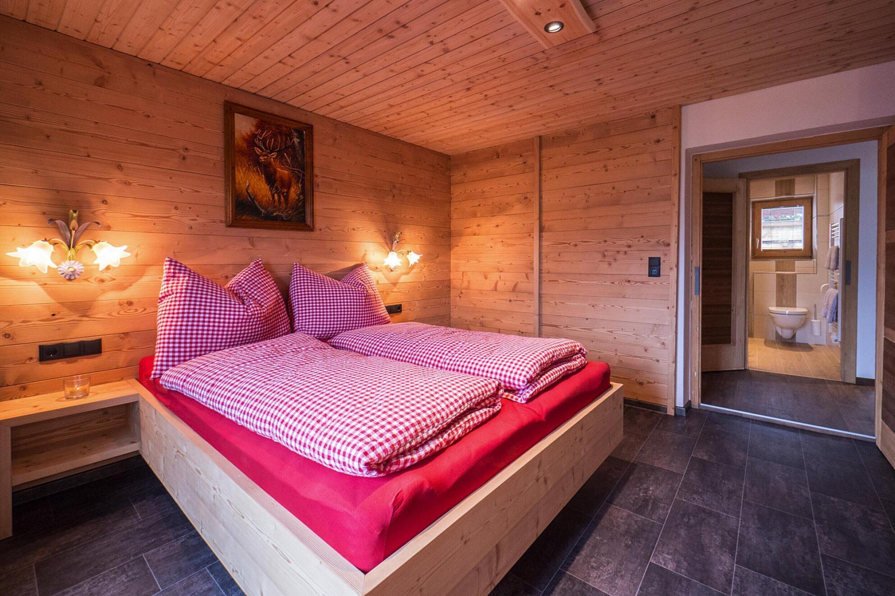 A wooden cabin bedroom with a bed, bedside lamps, and a painting on the wall.