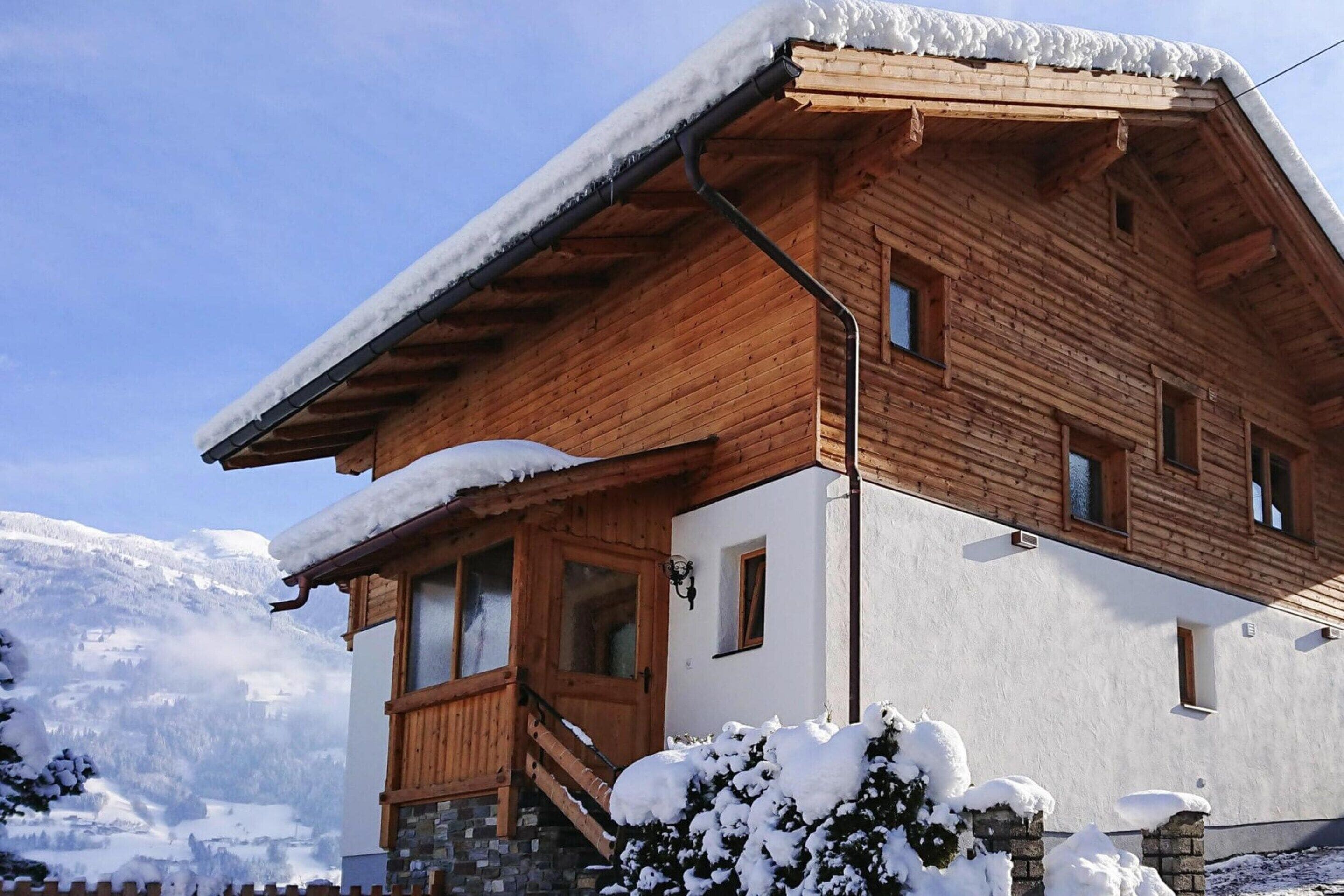 Een houten chalethut met een schuin dak, een balkon en uitzicht op besneeuwde bergen.