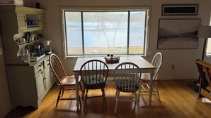 A kitchen with a large window overlooking a lake, wooden cabinets, and a dining table with chairs. - Lake Cottage - Put your Feet up and Relax! (Moultonborough)