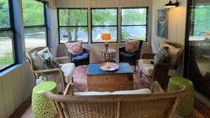 A cozy room with wicker furniture, a wooden ceiling, and large windows offering a view of the outdoors. - Lake Cottage - Put your Feet up and Relax! (Moultonborough)