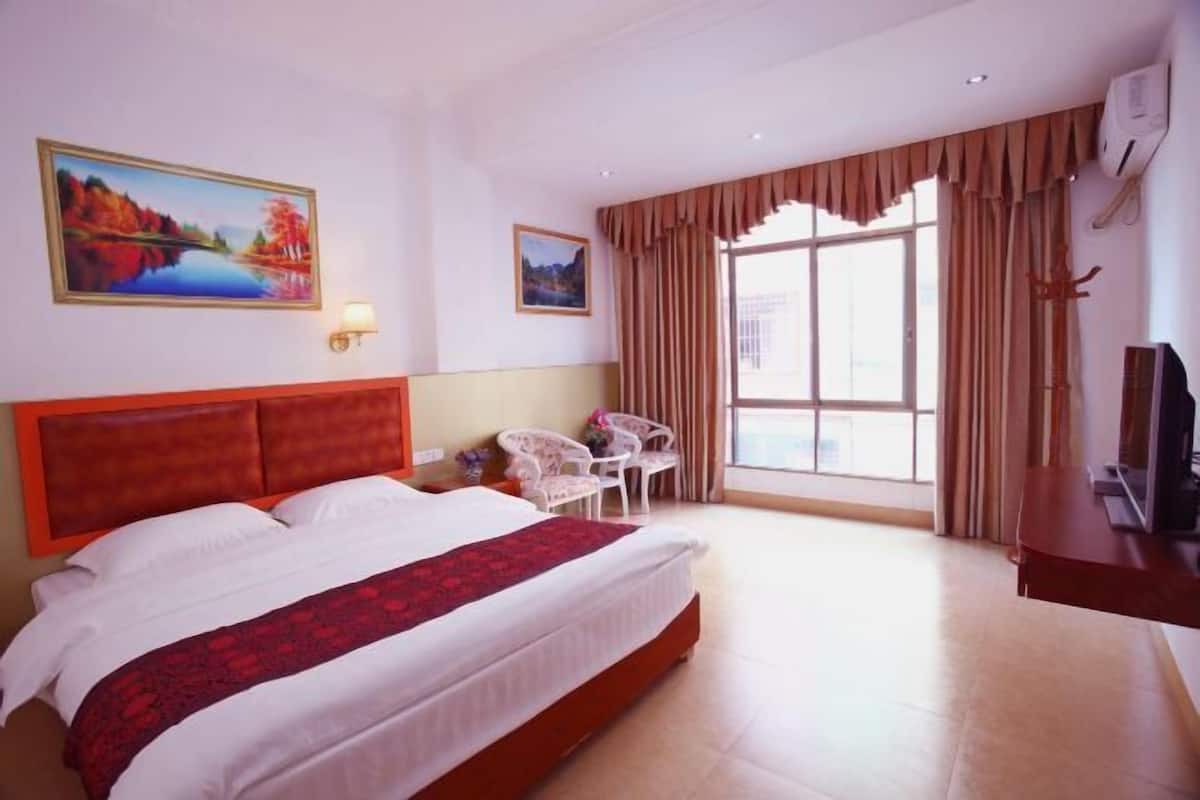 Habitación de hotel con una cama grande, un escritorio, una silla, un televisor y una ventana con cortinas.
