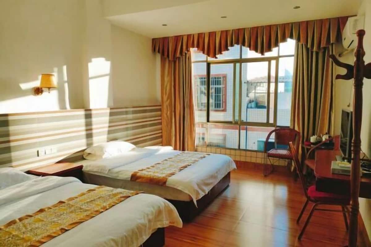 Habitación de hotel con dos camas, un escritorio, una silla y un ventanal con cortinas.