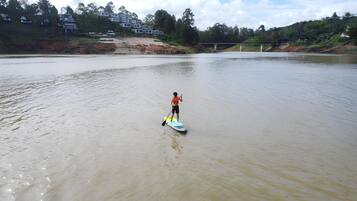 A person paddleboarding on a calm river with a bridge in the background.