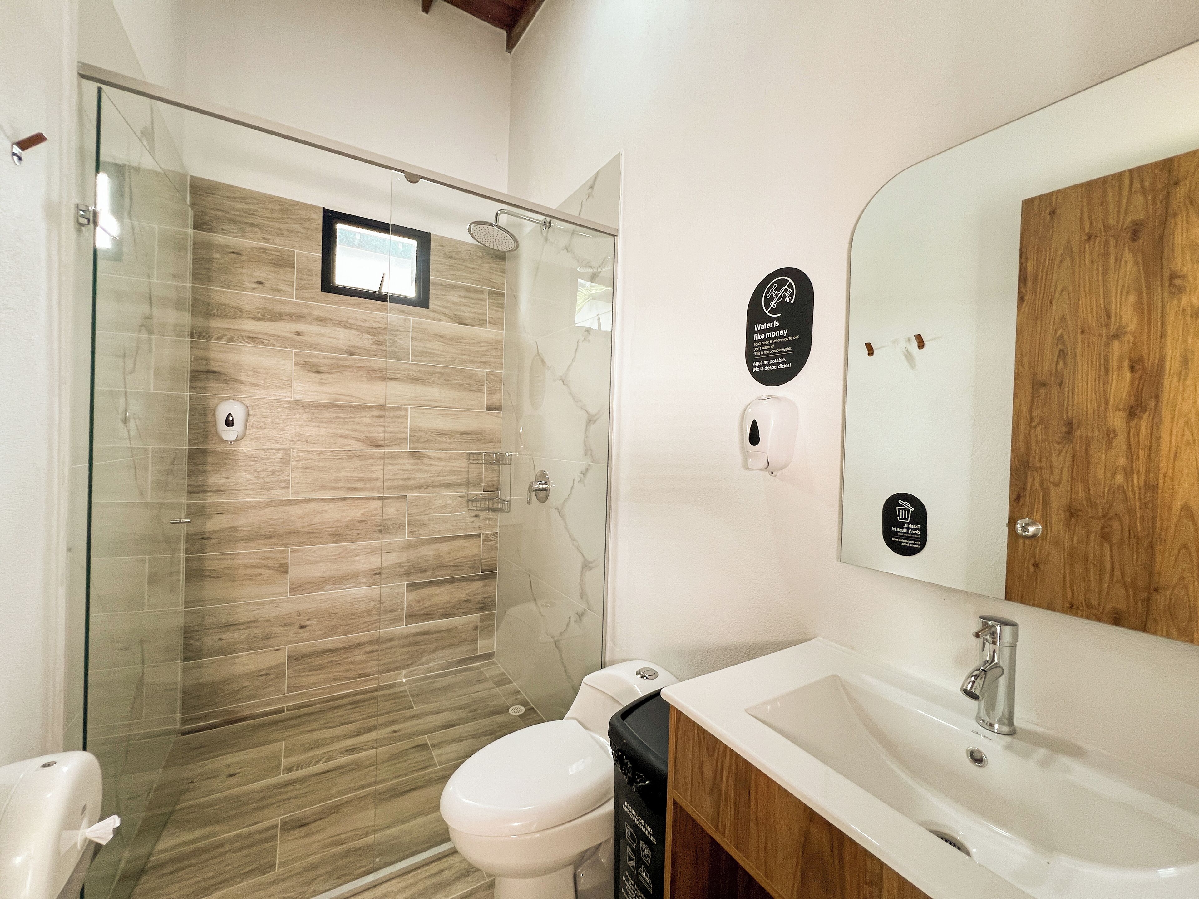 Ein modernes Badezimmer mit einer ein Glaswand trennenden Dusche, einem Holzwaschtisch und einem großen Spiegel.