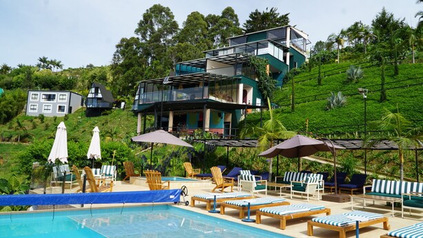 A pool area with lounge chairs and umbrellas, surrounded by lush greenery and modern buildings. - Viajero Guatapé Hostel & Lake Club (El Peñol)