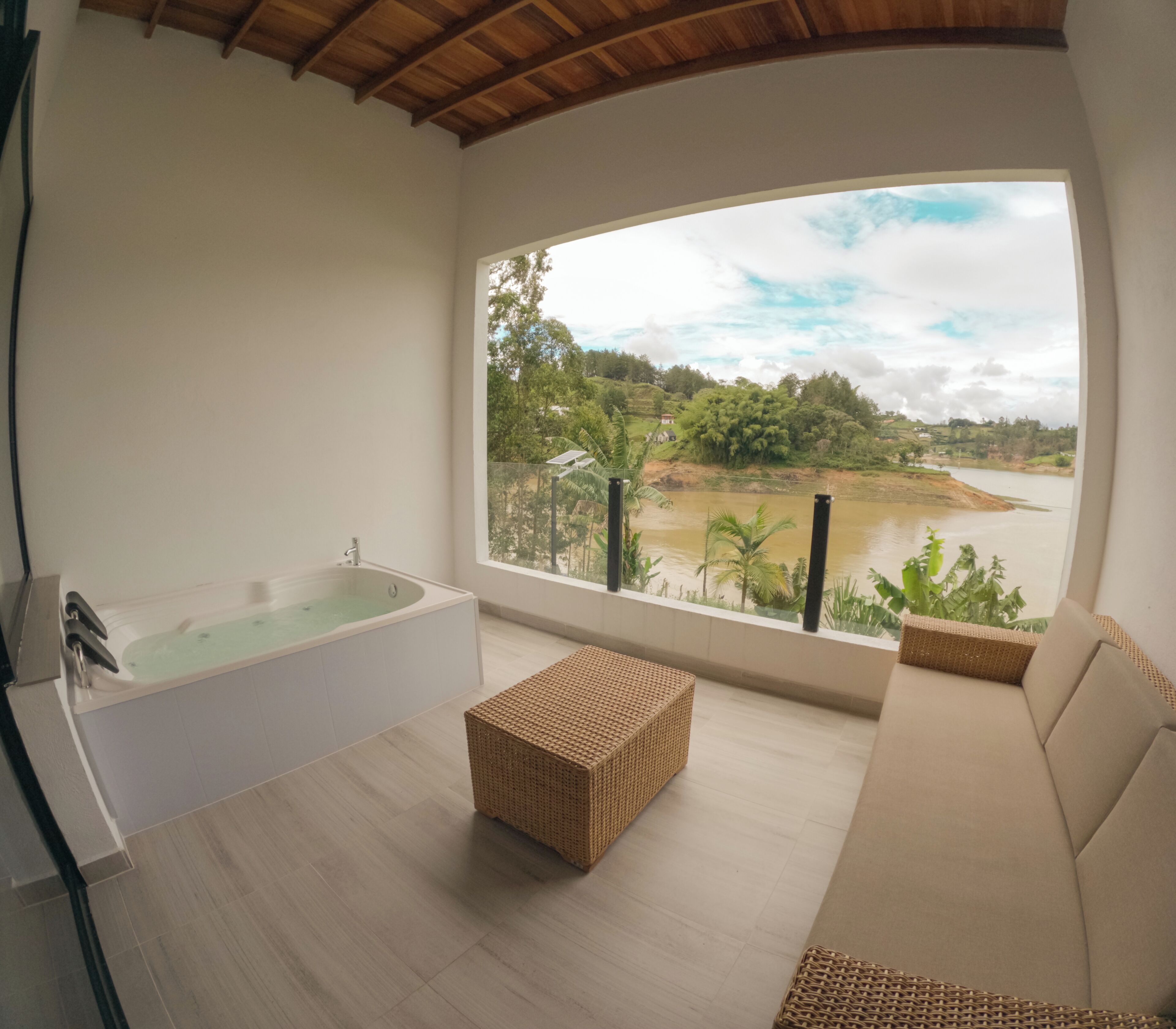 Un baño moderno con bañera, un reposapiés de mimbre y un sofá color beige.