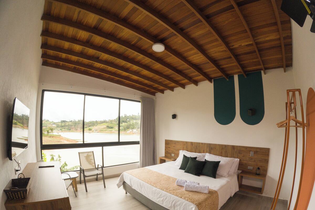 Une chambre à coucher avec un grand lit, un bureau, une chaise, une fenêtre donnant sur un beau paysage et un ventilateur de plafond.