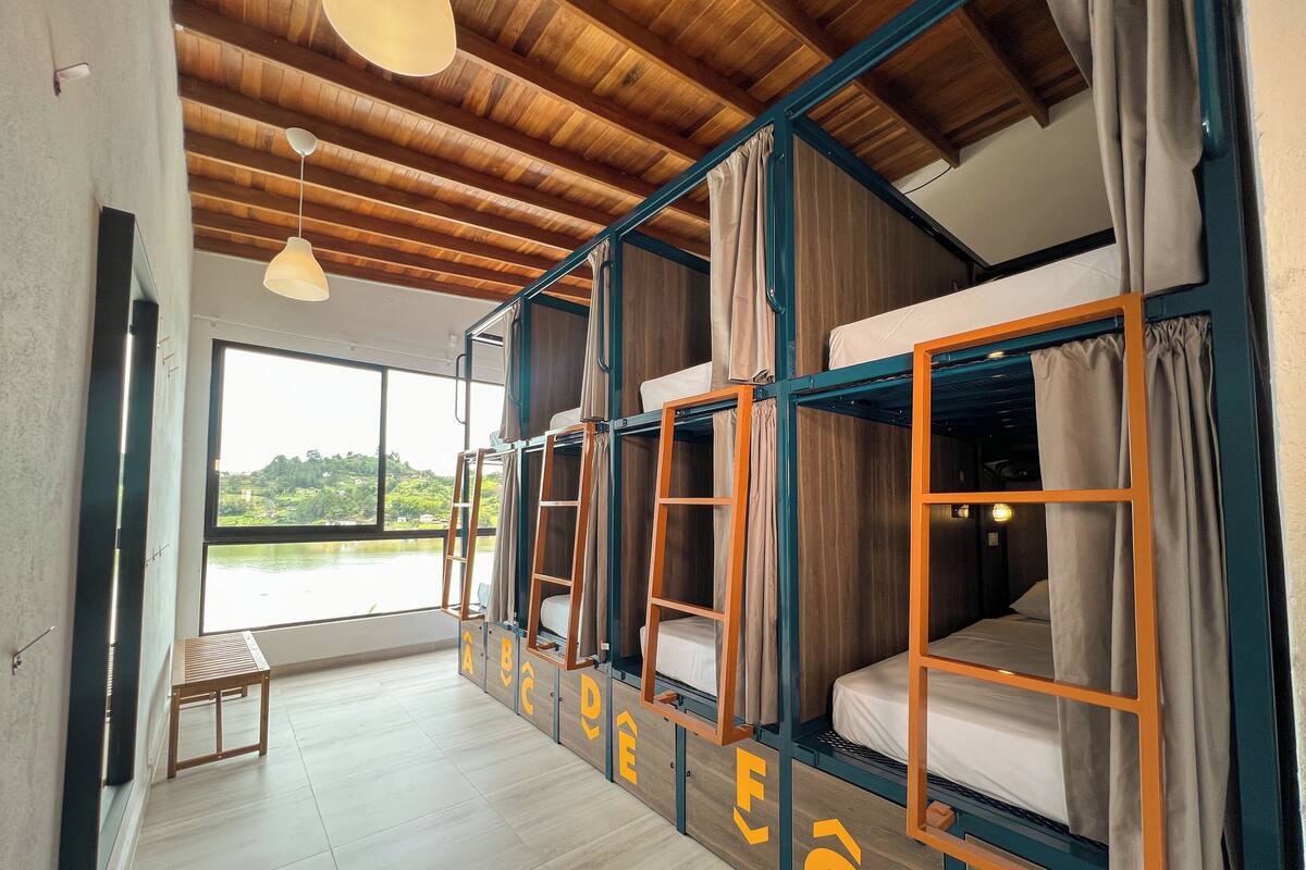 Une chambre de type dortoir, avec des lits superposés, un plafond en bois et une vue sur un lac.