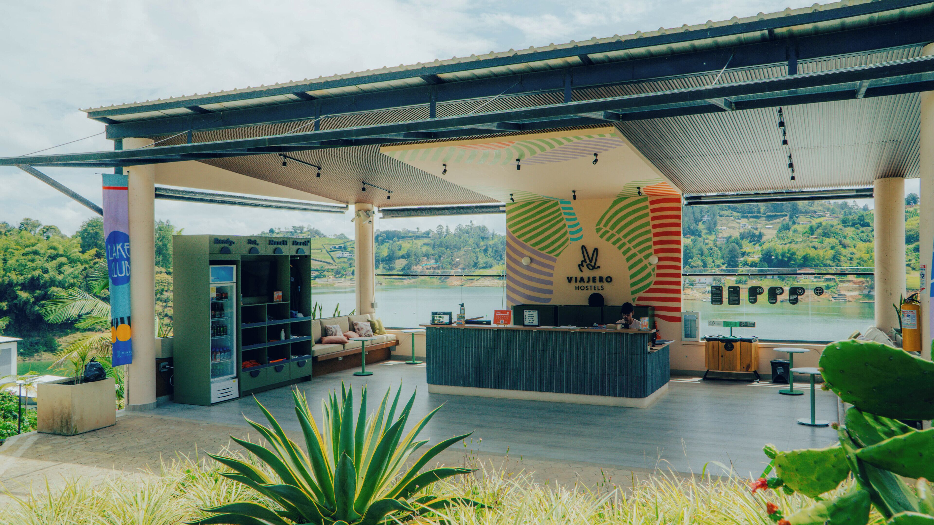 A modern hostel with a reception desk, seating area, and a view of a river.
