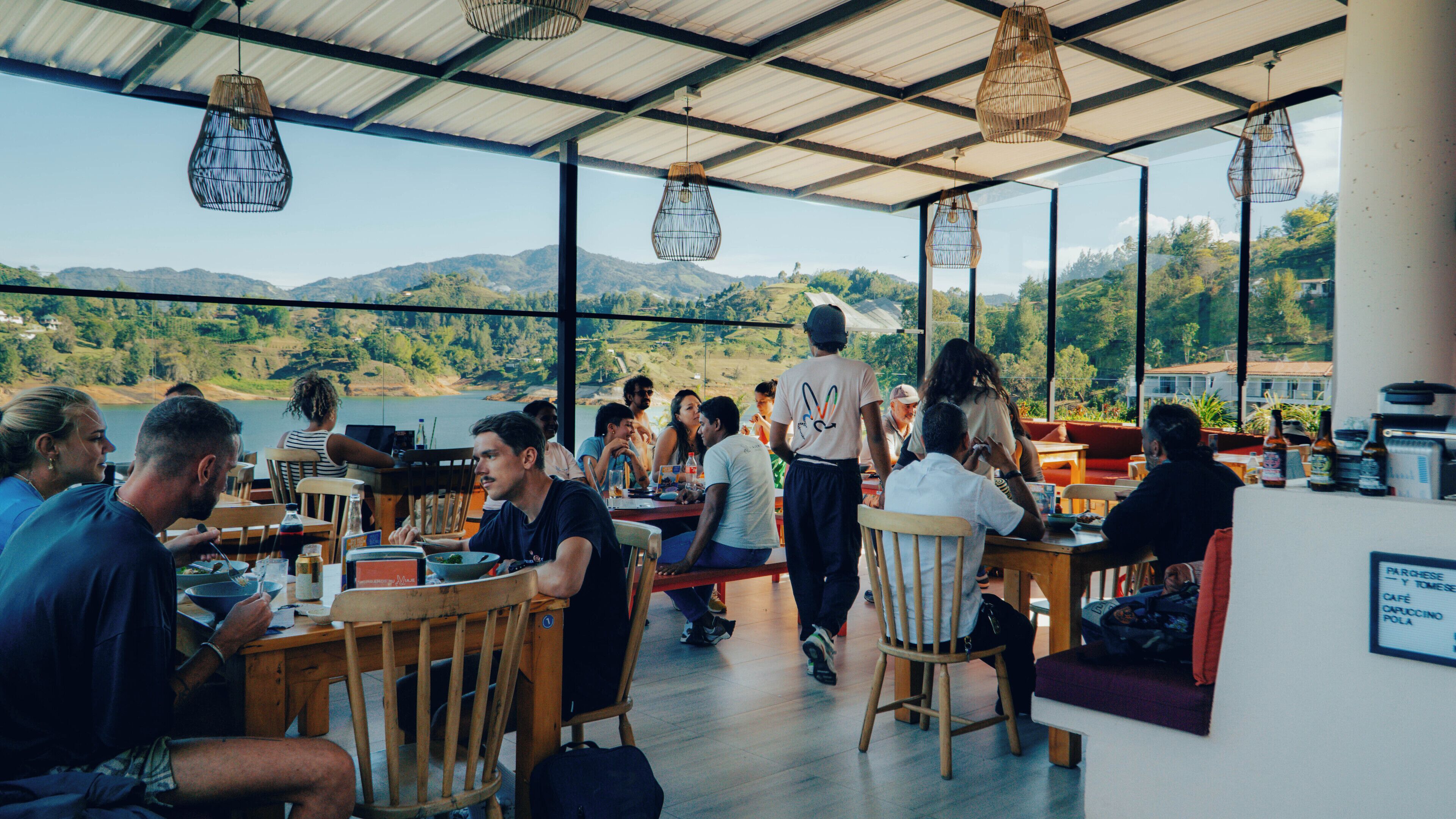 A restaurant with a view of the mountains and lake, wooden furniture, and hanging light fixtures.